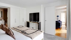 Ein Schlafzimmer mit einem Bett, einem Fernseher auf einem Schrank, einem Kleiderschrank und einer Tür zu einem anderen Raum.