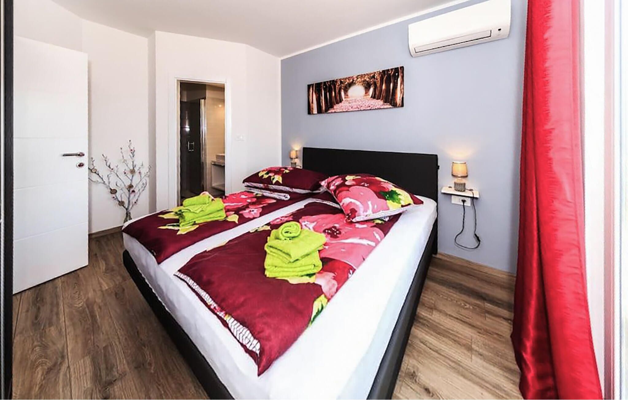 A hotel room with a bed, a door, a wall-mounted air conditioner, and a nightstand with a lamp.