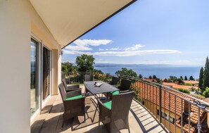 A balcony with a table and chairs, a view of the sea, and a building with red-tiled roofs. - 3 bedroom awesome apartment in Ika (Ika)