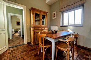 A dining area with a wooden table and chairs, a cabinet with glass doors, and a window with curtains. - Hoefke Voort – Rural farmhouse in Haspengouw, total peace in protected landscape (Tongeren-Borgloon)
