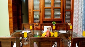 Un comedor con mesa de vidrio, sillas de madera, una cesta de frutas y una jarrón.