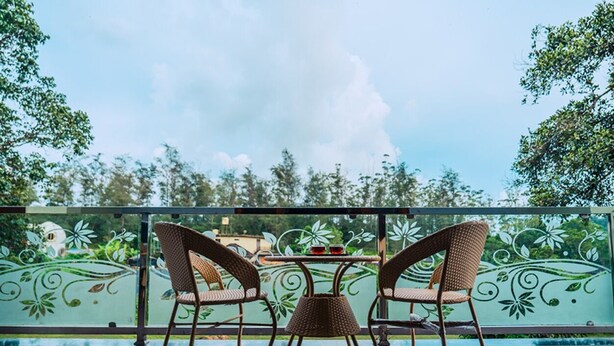 Un balcón con sillas de mimbre y una pequeña mesa, con vistas a un jardín con valla decorativa.