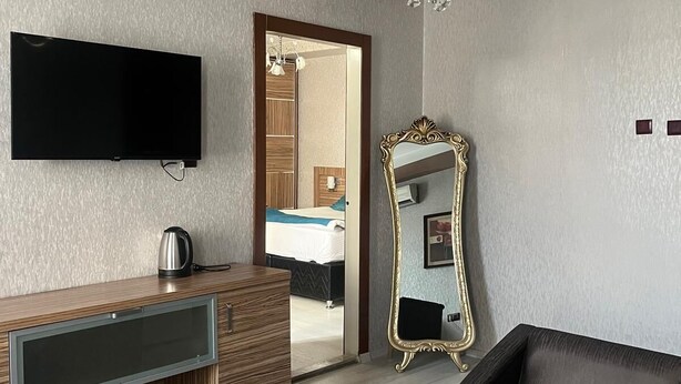 Un salon moderne doté d’un téléviseur à écran plat, d’un meuble de rangement en bois, d’un canapé en cuir noir, d’une table basse en verre, d’un grand miroir et d’un lustre.