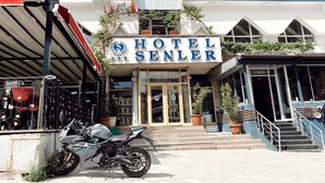 Un hôtel avec une enseigne indiquant « HÔTEL SENLER », une moto garée devant et un escalier menant à l’entrée.