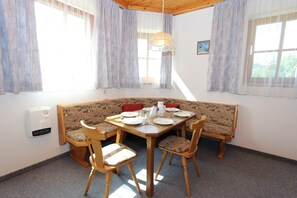 A dining area with a round table, four chairs, a bench, and a window with curtains.