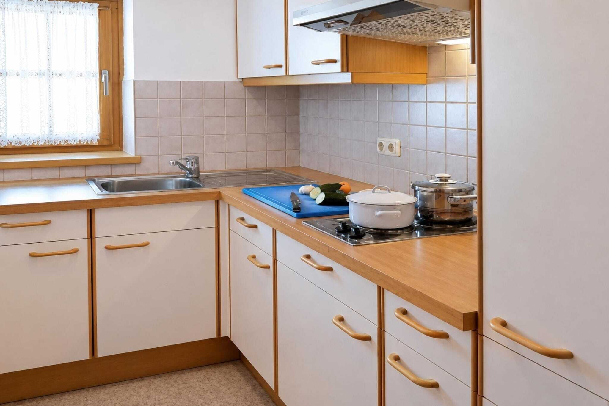 A kitchen with white cabinets, wooden handles, a sink, a stove, and a window with a lace curtain.