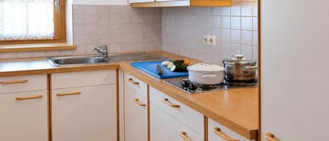 A kitchen with white cabinets, wooden handles, a sink, a stove, and a window with a lace curtain.