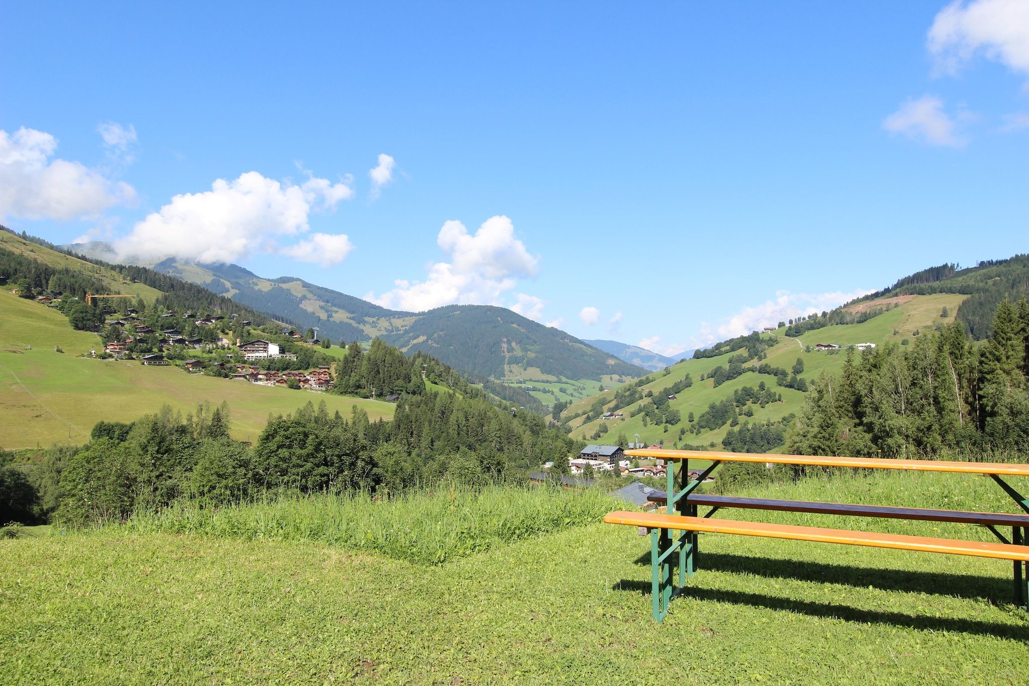 A picnic table in a grassy field with a view of a valley and mountains in the background.