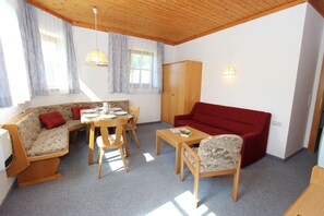 Ein möbliertes Wohnzimmer mit Sofa, rotem Sitzsofa, Esstisch mit Stühlen und einem Holzschrank.