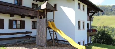 A building with a wooden balcony, a yellow slide, and a climbing wall.