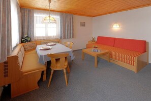 Ein gemütliches Zimmer mit Esstisch, Stühlen, einer Couch und einem kleinen Tisch mit einer Obstschale.