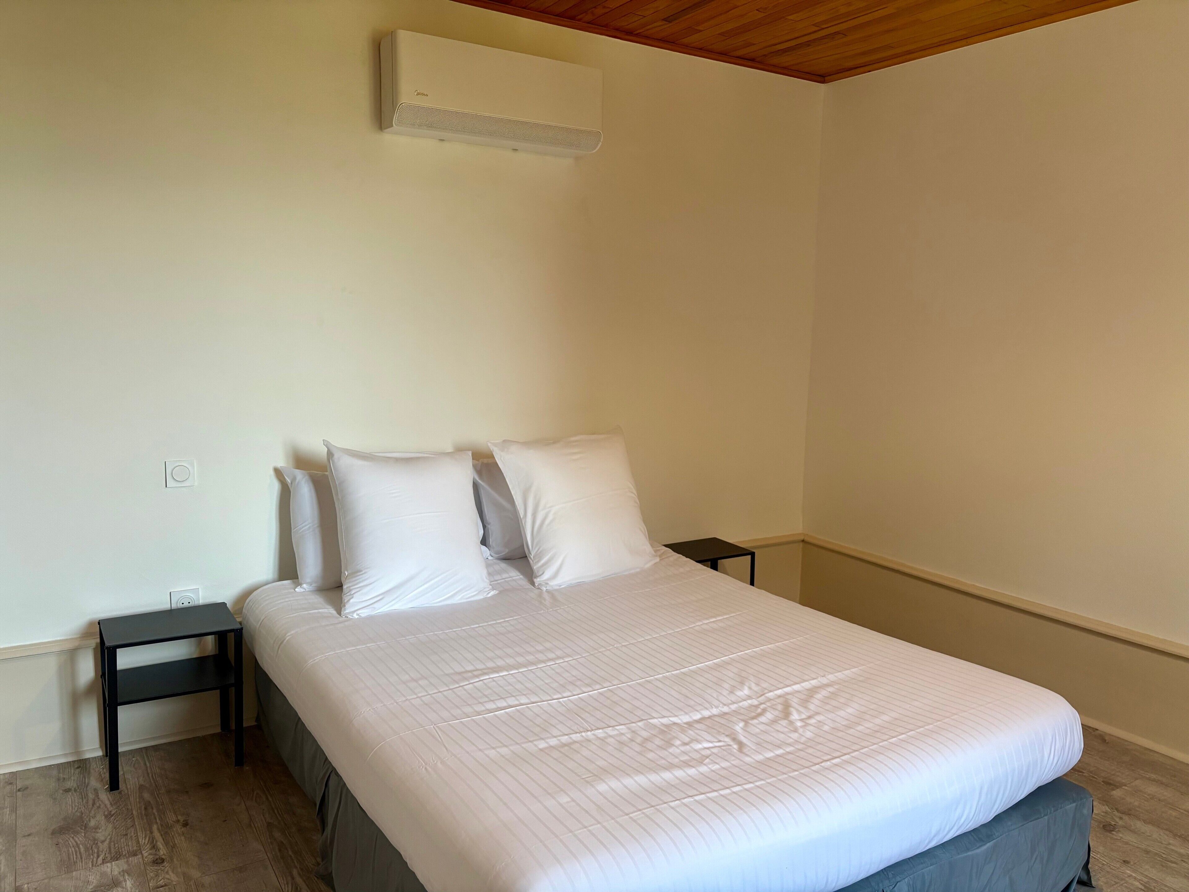 Ein Schlafzimmer mit einem Bett, zwei Nachttischen, einer Wand-Klimaanlage und einer Holzzieldecke.