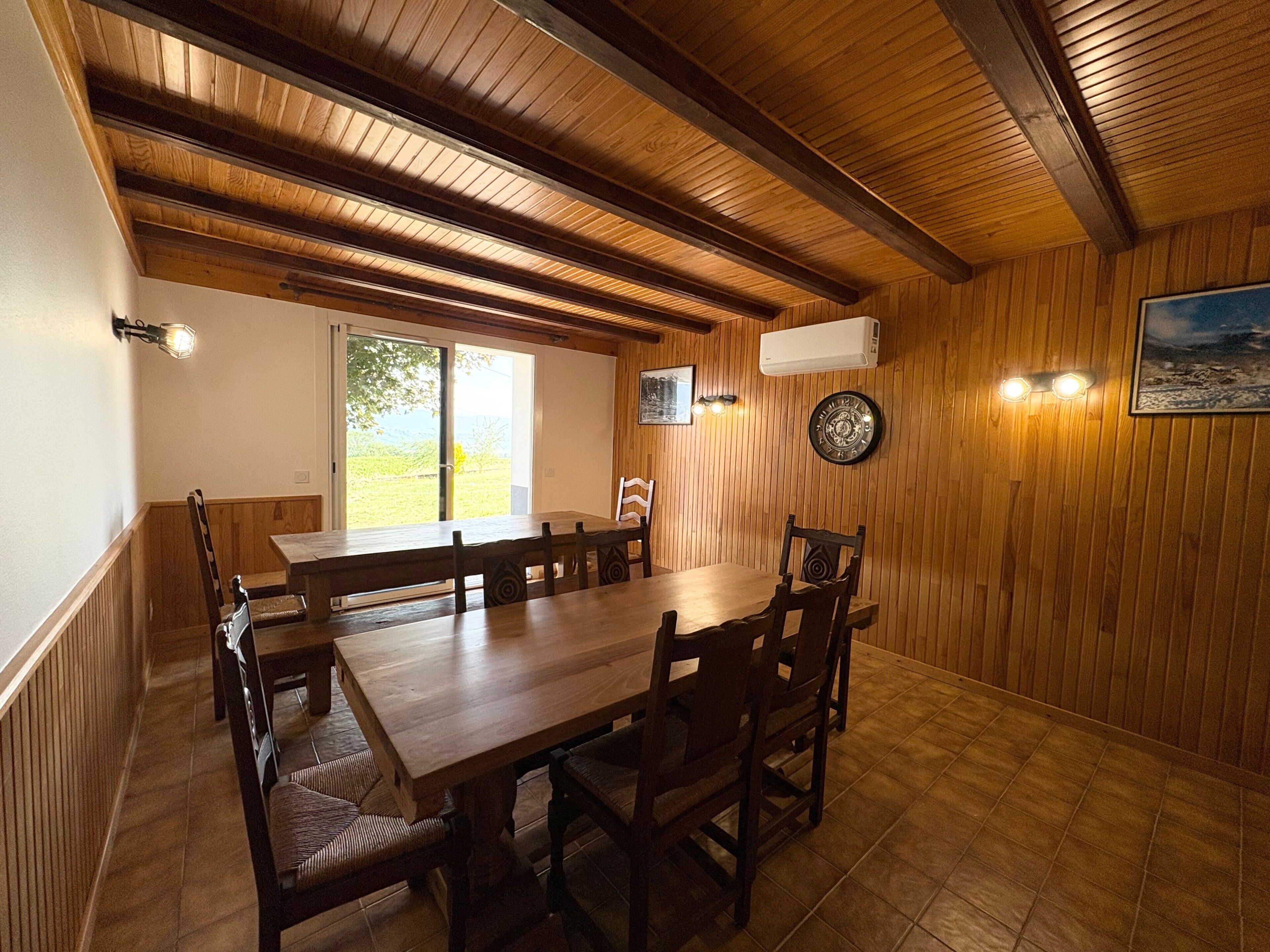 Ein Holzinterieur mit einem Esstisch, Stühlen, einer Uhr und einer Wand-Klimaanlage.