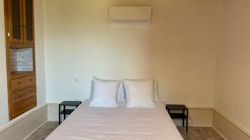 Une chambre à coucher comprenant un lit, une armoire en bois, des tables de chevet et un appareil de climatisation.
