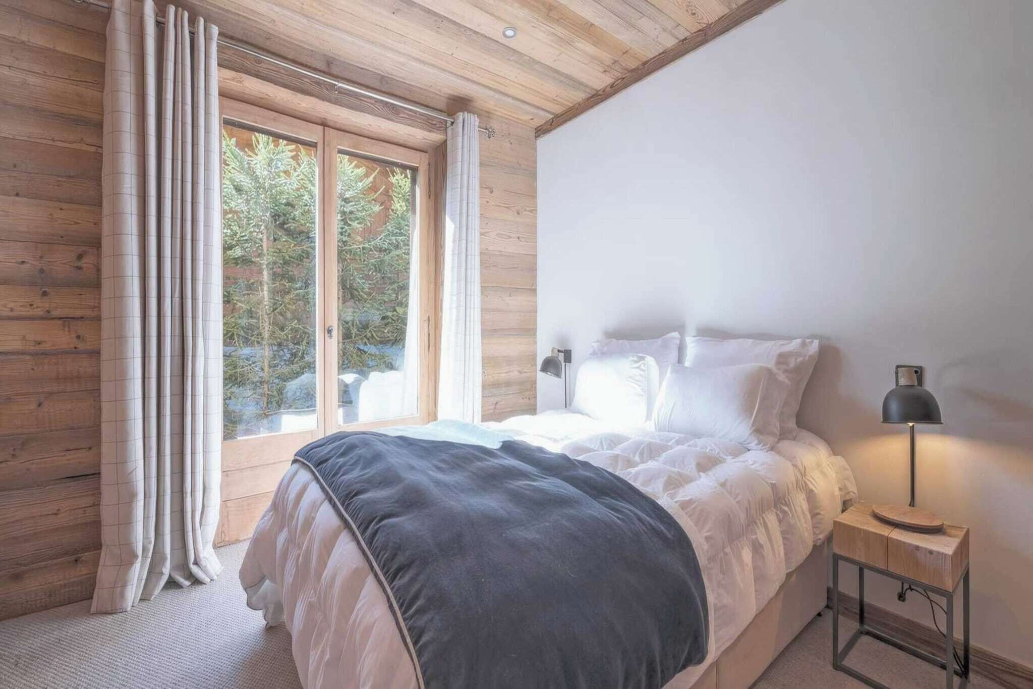 Een slaapkamer met een bed, nachtkastje, lamp en een raam met gordijnen.