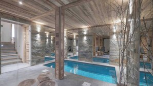 Ein Schwimmbecken mit Steinsäulen und Holzbalken, eine Treppe und eine Sitzgelegenheit mit runden Holzsitzen.