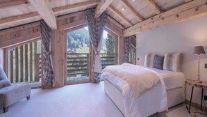 Ein Schlafzimmer mit einem großen Bett, einem Sessel, einem Nachttisch und einem Fenster mit Vorhängen.