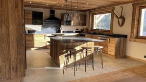 Eine moderne Küche mit Holzschränken, einer großen Kochinsel mit Sitzgelegenheiten, Pendelleuchten und einer Dekoration mit einem Hirschschädel.