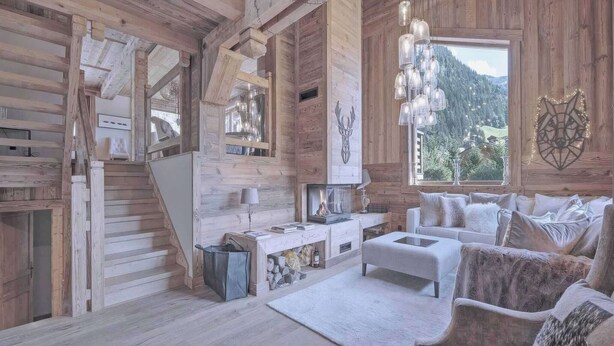 Ein Holzinnenraum mit Kamin, einer Couch und Blick auf eine Berglandschaft.