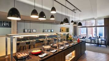 A modern hotel breakfast area with a buffet, pendant lighting, and seating.