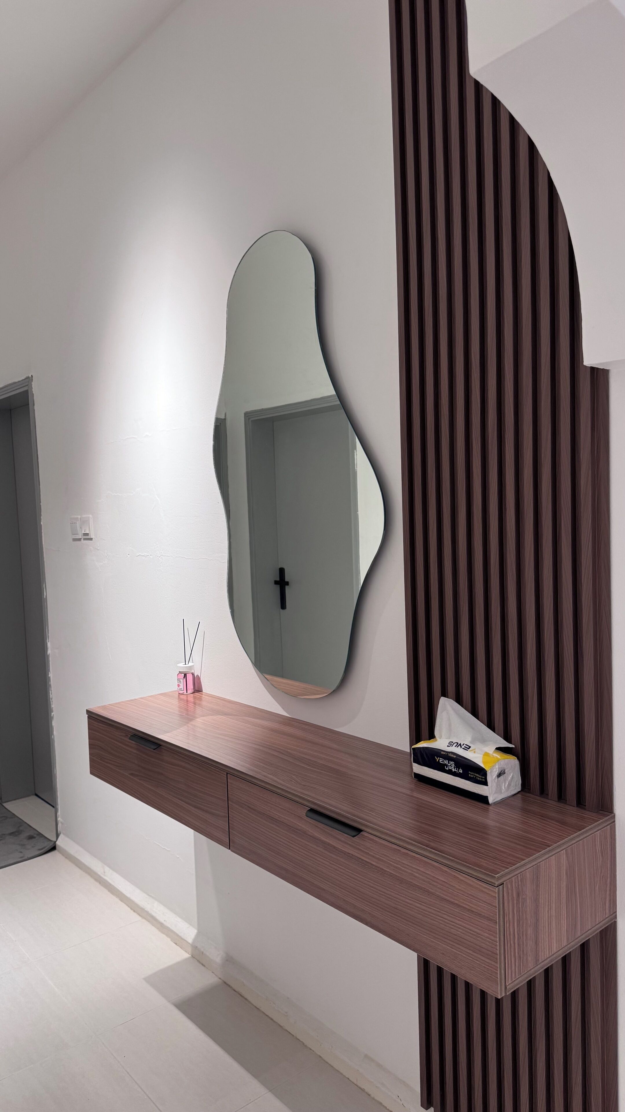 Een moderne badkamer met een houten wastafelmeubel, een grote spiegel en een wandpaneel ontwerp.