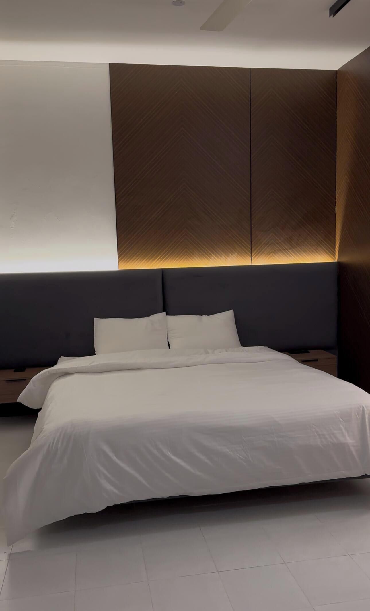 A modern bedroom with a large bed, dark headboard, and a wall with a geometric pattern.