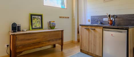 Una cocina con un banco de madera, un refrigerador, una ventana con persianas y una puerta.