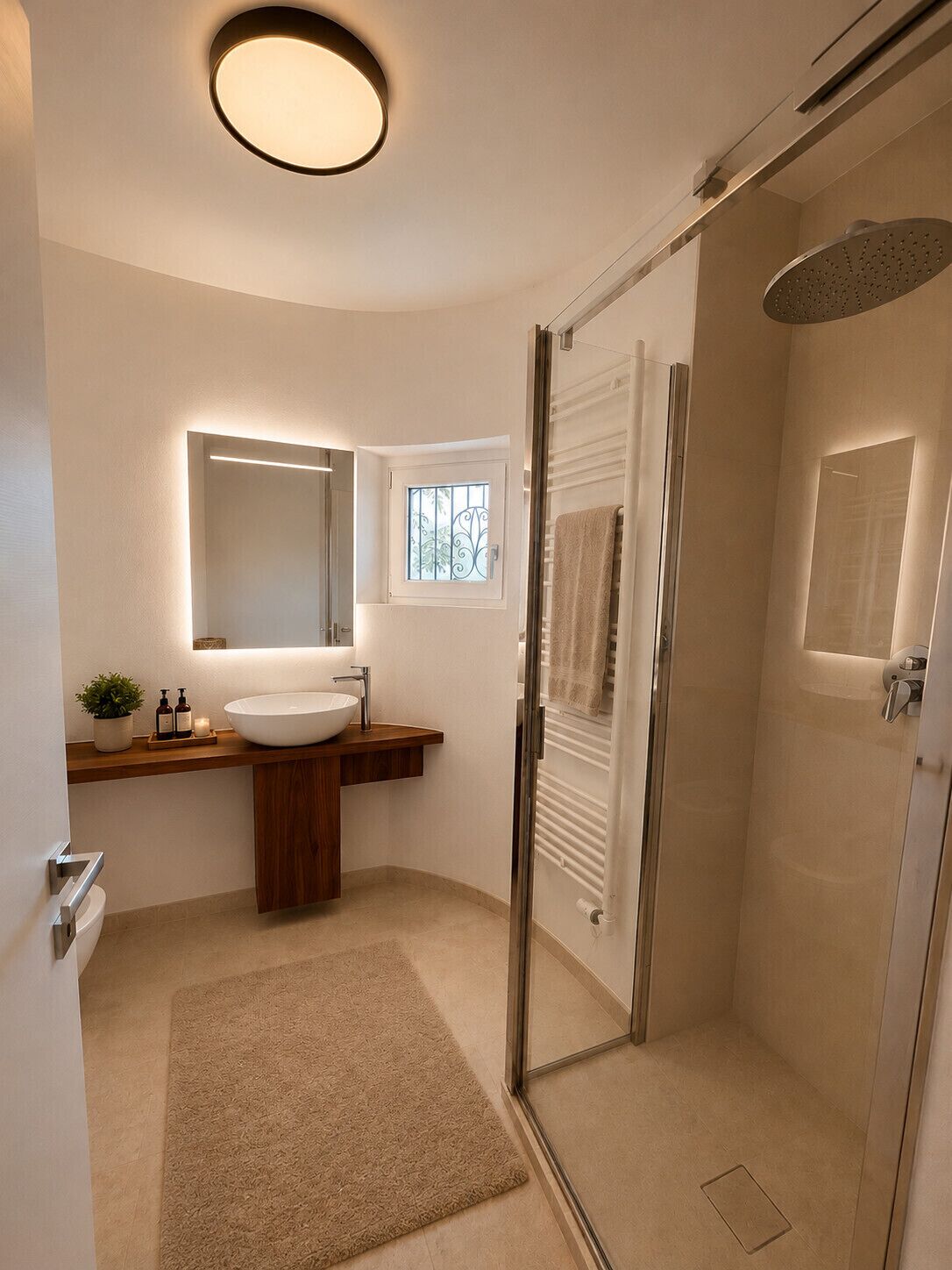 A modern bathroom with a large sink, a mirror, a shower, and a small window.