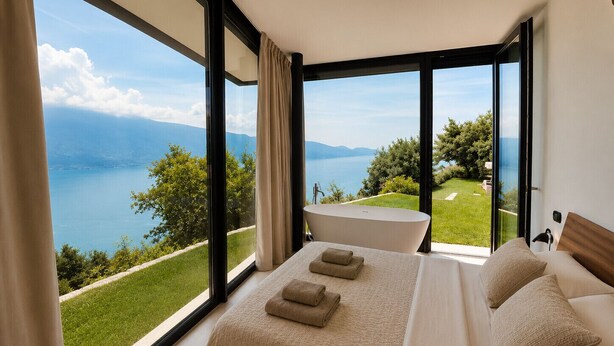 Una camera da letto con un grande letto, vista su un lago e un balcone.