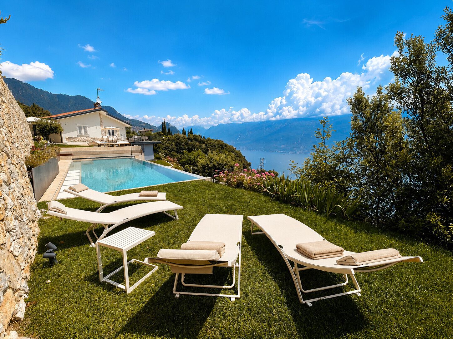 Un espace aménagé au bord de la piscine, avec des chaises longues, une piscine et une vue sur les montagnes et un lac.