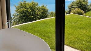 Un bagno moderno con una vasca da bagno ampia, vista su un lago e un'area verde esterna.