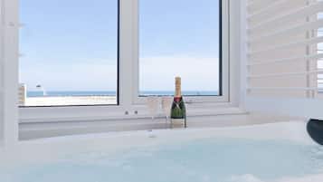 A room with a large window, a hot tub, and a bottle of champagne.