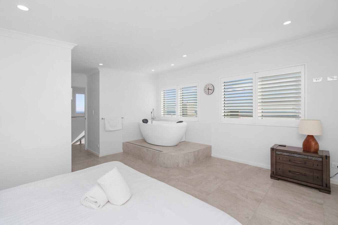 A modern bedroom with a large bed, a bathtub, and a wooden dresser.