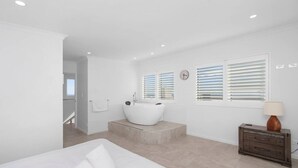 Ein modernes Schlafzimmer mit einem großen Bett, einer Badewanne und einer Holzkommode.