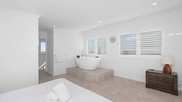 A modern bedroom with a large bed, a bathtub, and a wooden dresser.