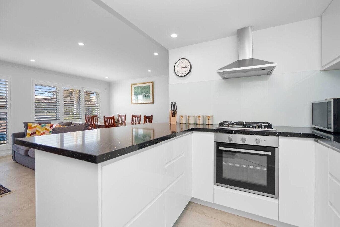 A modern kitchen with a central island, built-in oven, stainless steel range hood, and a microwave.