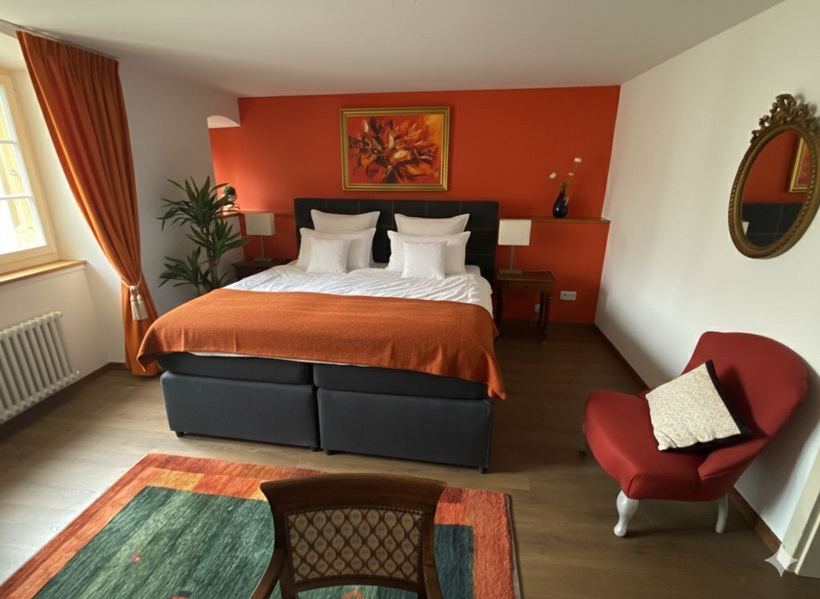 A bedroom with a bed, a chair, a mirror, and a painting on the wall.