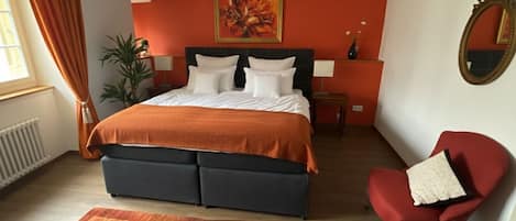 A bedroom with a bed, a chair, a mirror, and a painting on the wall.
