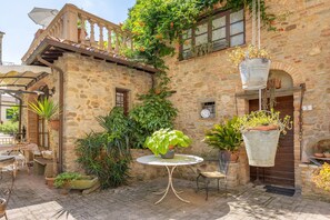 Ein Steinhaus mit Balkon, hängendem Blumentopf, rundem Tisch und Topfpflanzen.