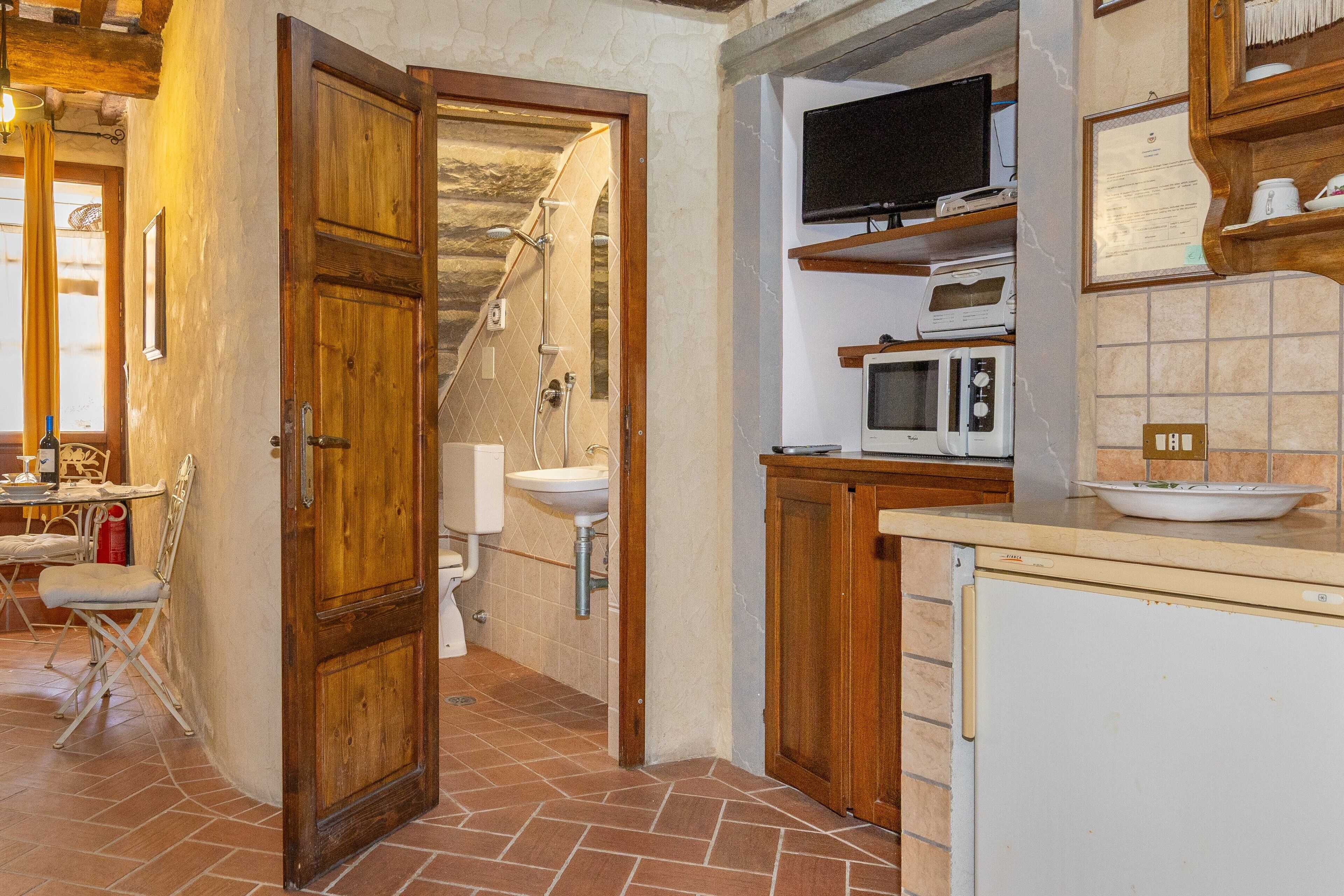 A kitchen with a wooden door, a sink, a microwave, and a television on a shelf.