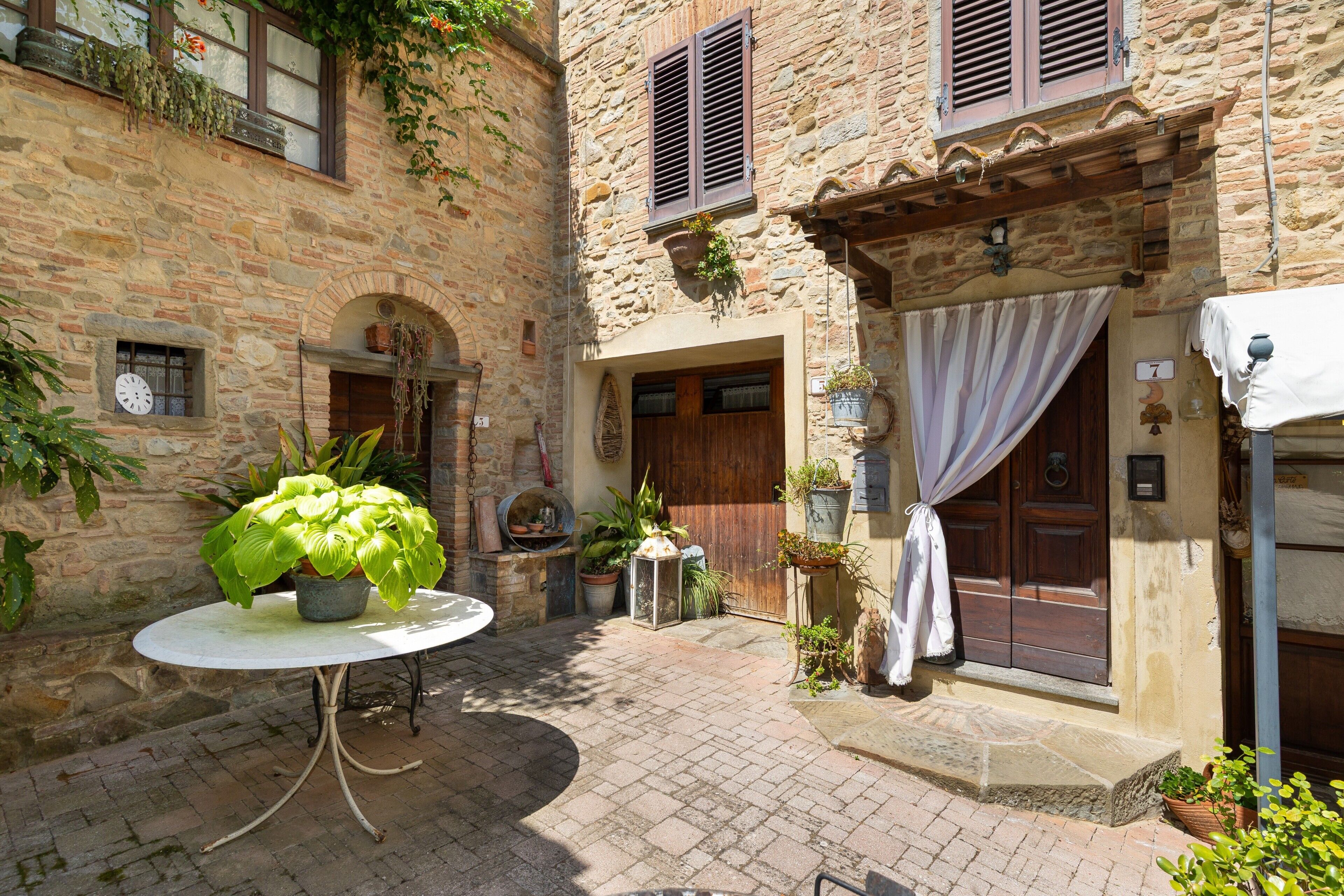 A courtyard with a round table, potted plants, a wooden door, and stone walls.