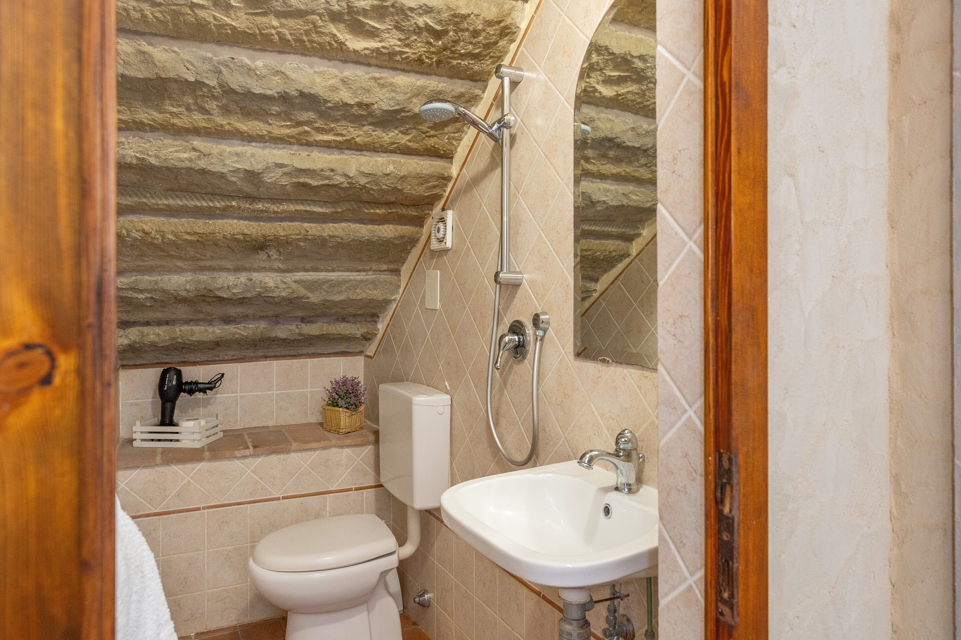 A bathroom with a toilet, sink, shower, and a stone wall.