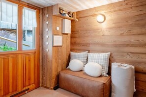 A cozy room with a wooden wall, a bench with pillows, a shelf with decorative items, and a window with curtains. - Les Évouettes - Châtel Village (Châtel)