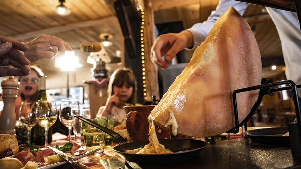 Una persona che taglia una grande fetta di carne su un tavolo con diversi cibi e bicchieri di vino.