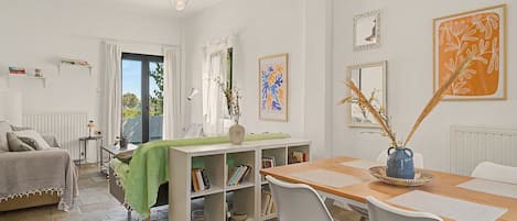 A well-lit room with a dining table, chairs, a bookshelf, and a window with curtains.