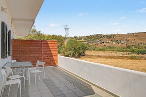 Een balkon met een tafel en stoelen, een houten omheining en uitzicht op een heuvel met gebouwen.