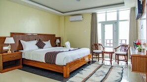 Habitación de hotel con cama de madera, dos mesitas de noche, un escritorio con silla y un ventanal grande.