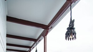Un balcón techado con barandilla de metal, lámparas colgantes y vista a un paisaje montañoso.
