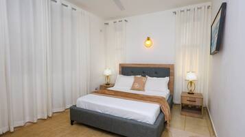 A hotel room with a bed, two bedside tables, a ceiling fan, and a wall-mounted light fixture.