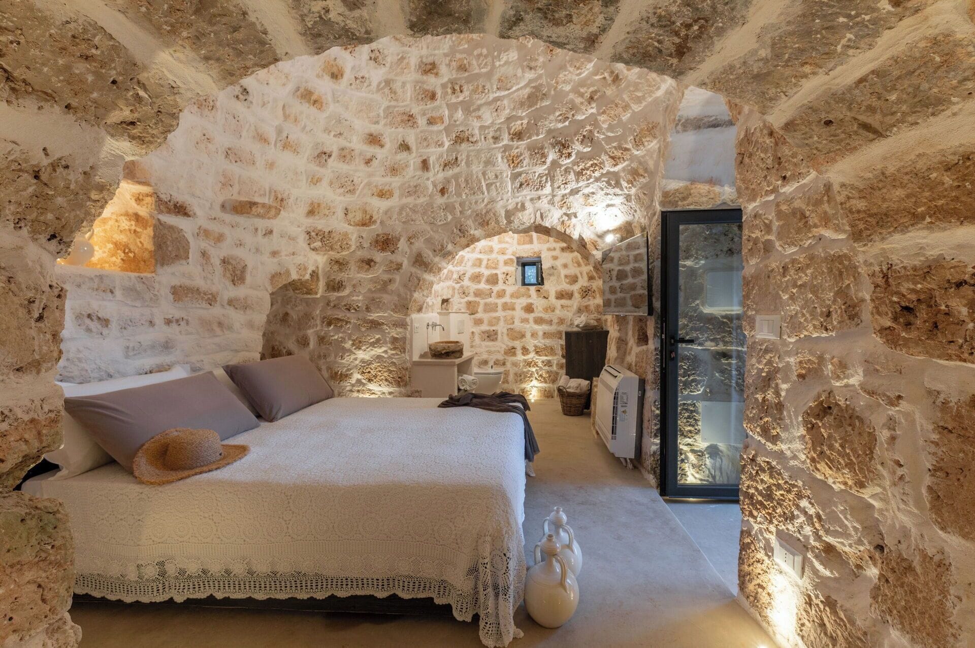A stone-walled bedroom with a bed, a small window, and a bathroom.
